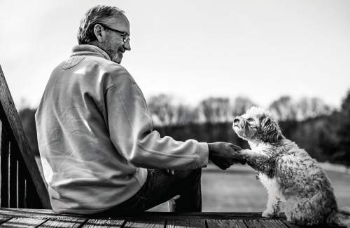 Dave sits on his porch holding his dogs paw as he shakes